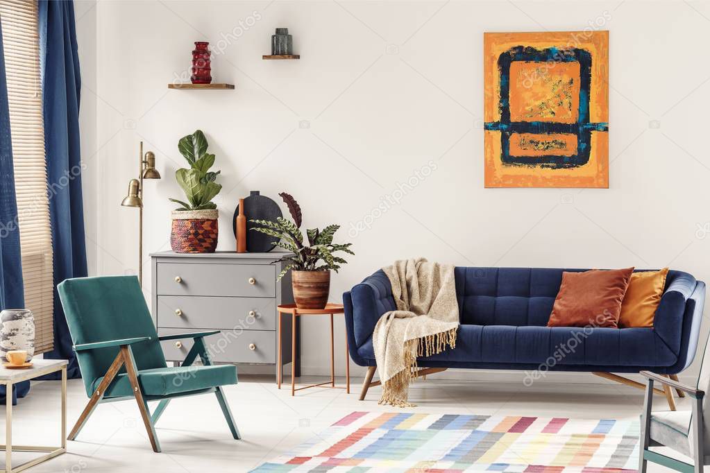 Orange end table with fresh plant standing next to navy couch wi