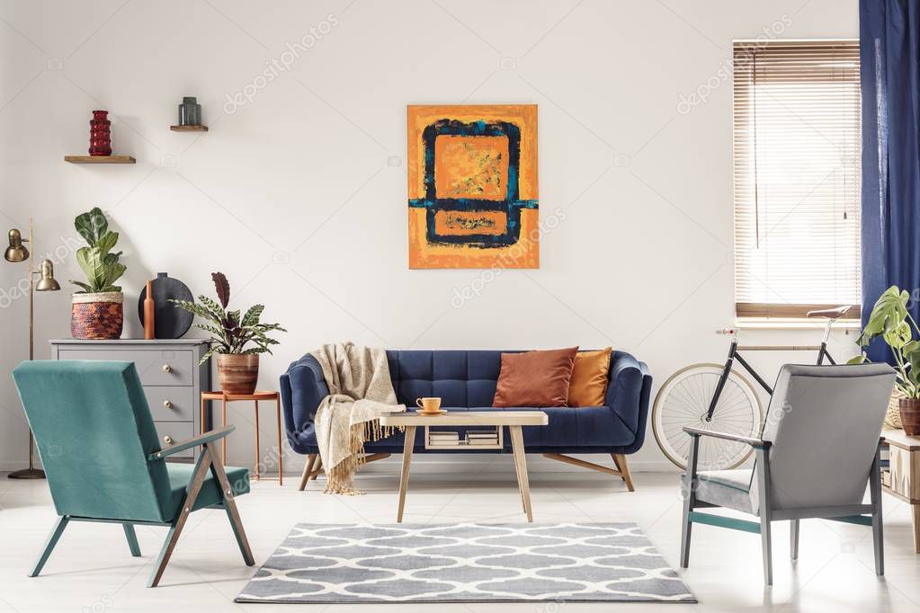 Real photo of a navy blue sofa with orange cushions and an artwo