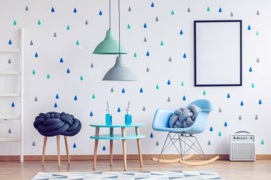 Mavi, nane ve ahşap mobilya ve duvarda mockup posteri ile İskandinav çocuk oyun odasında mavi sandalyeye düğüm yastık