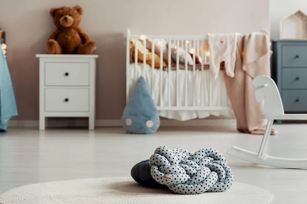 Close-up em uma almofada de nó com padrão de pontos deitado em um tapete branco. Quarto de bebé desfocado ao fundo. Foto real — Fotografia de Stock