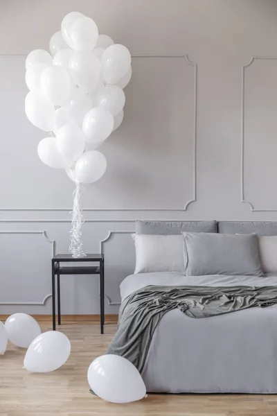 Copiar el espacio en la pared gris vacía del elegante interior del dormitorio con una cama acogedora y un montón de globos blancos —  Fotos de Stock