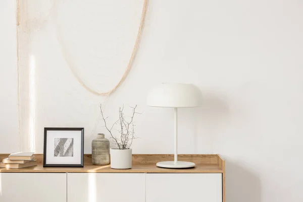 Bílá průmyslová lampa, fotografie v rámu a rostlina v hrnci na dřevěném stolku v elegantní obývací místnosti s bílou zdí — Stock fotografie