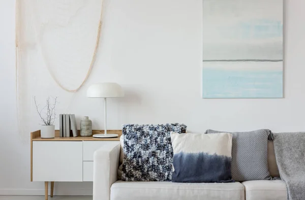 Абстрактная сине-белая роспись на пустой белой стене за бежевым диваном с подушками — стоковое фото