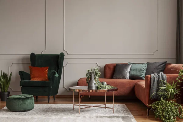 Оксамитове смарагдове зелене крісло з помаранчевою подушкою поруч з кутовим диваном і журнальним столиком — стокове фото