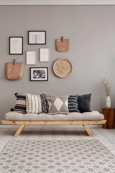Flores secas em vaso branco em pequena mesa de madeira atrás confortável sofá futon com travesseiros — Fotografia de Stock