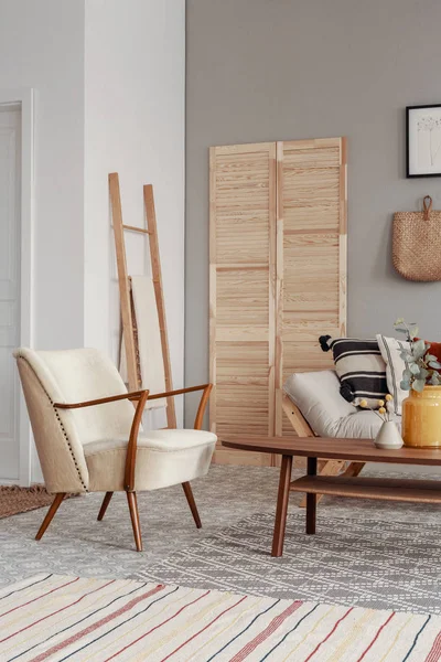 Стильное винтажное кресло в современном интерьере гостиной с диваном-кроватью и деревянной скандинавской лестницей с одеялом — стоковое фото