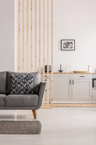 Open plan living room and kitchen interior with white cupboards and grey sofa with pillows