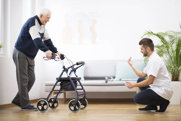 Oudere grootvader met Walker probeert weer te lopen en behulpzame mannelijke verpleegster die hem ondersteunt — Stockfoto