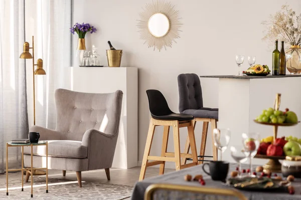 Trendy grijze fauteuil naast twee zwarte houten barkrukken in modieuze keuken en eetkamer interieur — Stockfoto