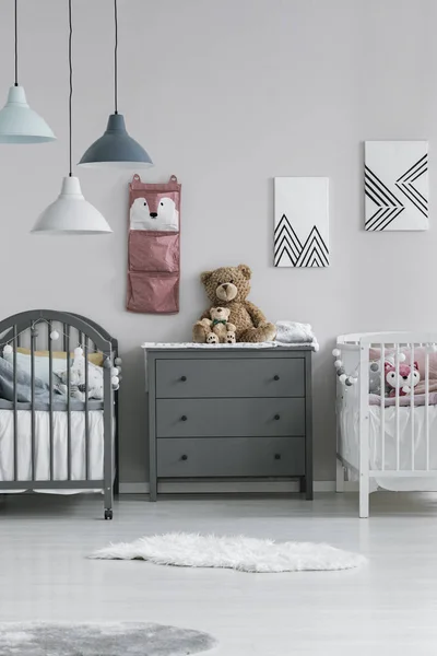 Απλό, γκρι και λευκό δωμάτιο εσωτερικό για δύο μικρά παιδιά με ένα σεντούκι συρτάρια μεταξύ δύο ξύλινων κρεβατιών. Πραγματική φωτογραφία — Φωτογραφία Αρχείου