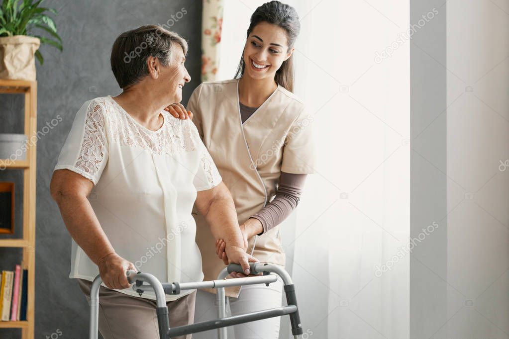 Smiling pretty nurse and disabled old lady with walker at home