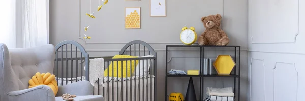 Panoramiczny widok uroczy żółty i szary Baby sypialnia z wygodnym fotelem i drewnianym łóżeczku — Zdjęcie stockowe