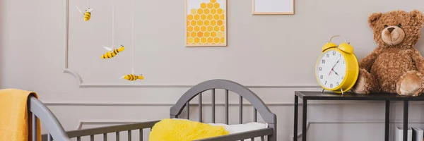 Vista panorámica del lindo dormitorio de bebé amarillo y gris con oso de peluche y reloj en estante de madera negro — Foto de Stock