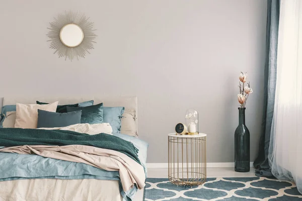 Orologio e fiore in vaso fantasia sul comodino accanto alla camera da letto king size con lenzuola verde smeraldo e beige — Foto Stock