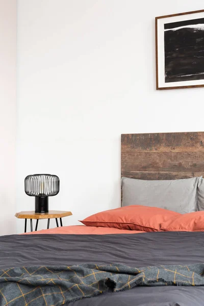 Close up of lamp on wooden nightstand and black poster on the white wall of elegant bedroom interior with king size bed with wooden headboard — стоковое фото