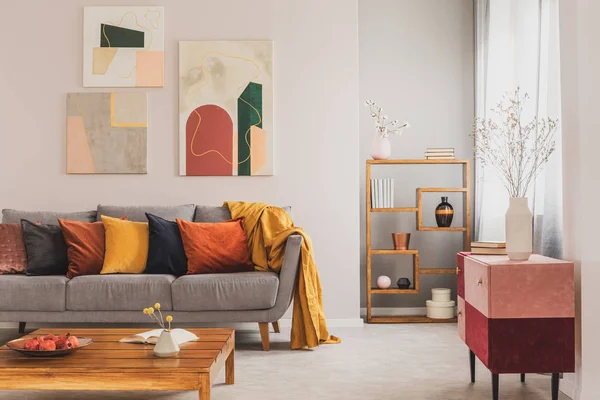 Yellow, orange, black and brown pillows on comfortable grey scandinavian sofa in bright living room interior with abstract paintings on the wall — Stock Photo, Image