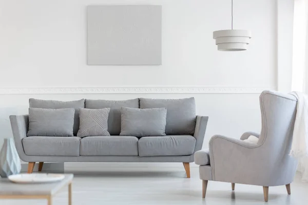 Grande poltrona posteriore ala confortevole accanto al lungo divano scandinavo grigio con cuscini in luminoso soggiorno interno — Foto Stock