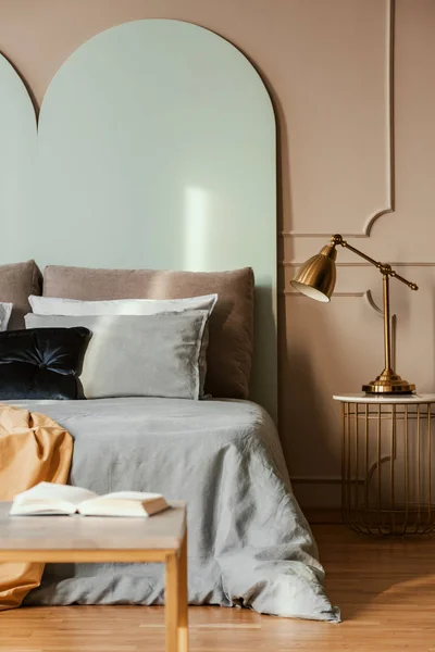 Gouden lamp op moderne nachtkastje tafel naast blauw bed in grijs slaapkamer interieur — Stockfoto