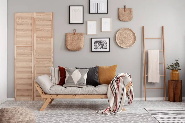 Træ og vidjer tilbehør i fashionable skandinavisk stue interiør med futon sofa med puder - Stock-foto