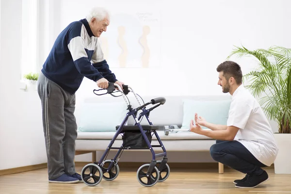 Nonno anziano con walker che cerca di camminare di nuovo e utile infermiere maschile che lo sostiene — Foto Stock