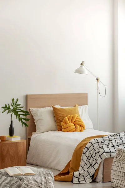 Knotenkissen und schwarz-weiße Decke auf Einzelbett in modischem Interieur mit grünem Blatt in Vase auf hölzernem Nachttisch — Stockfoto