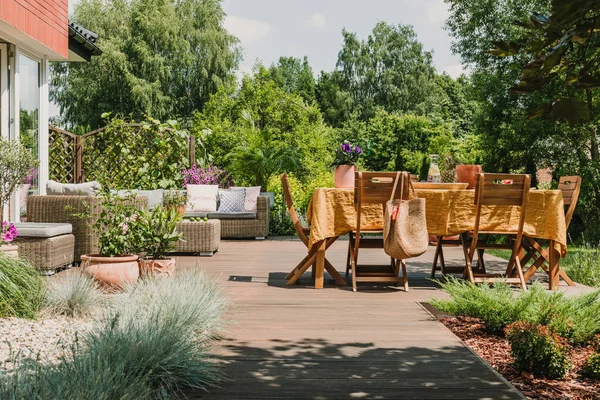 Esstisch mit orangefarbener Tischdecke auf Holzterrasse im grünen Garten — Stockfoto
