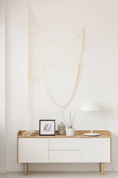 Белая промышленная лампа, фото в раме и растение в горшке на деревянном столе в элегантной гостиной с белой стеной — стоковое фото