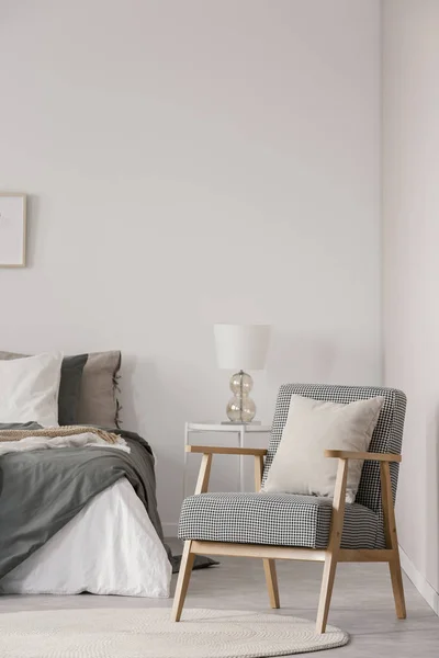 Кресло ретро с белой подушкой рядом с уютной двуспальной кроватью с серой кроватью в модном интерьере спальни — стоковое фото
