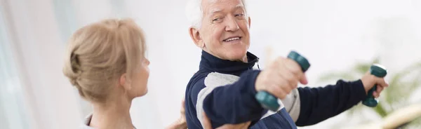 Hombre mayor después de un derrame cerebral en un hogar de ancianos haciendo ejercicio con un fisioterapeuta profesional — Foto de Stock