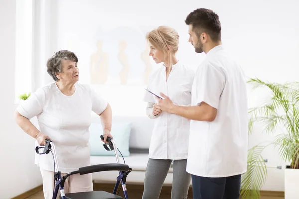 Šedá starší dáma s Walkere během rehabilitačního lékařství s profesionálním lékařem a mužskou ošetřovatelkou — Stock fotografie