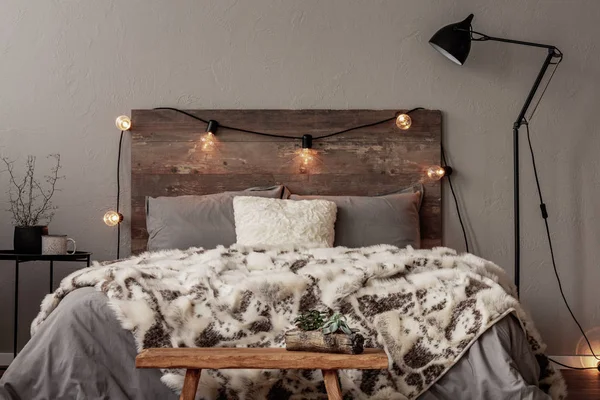 Light bulbs on wooden headboard of comfortable bed with grey bedding and warm fury blanket — Stock Photo, Image