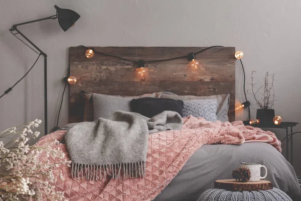 Сіра і пастельна рожева ковдра на сірій постільній білизні модної спальні з сільським дизайном — стокове фото