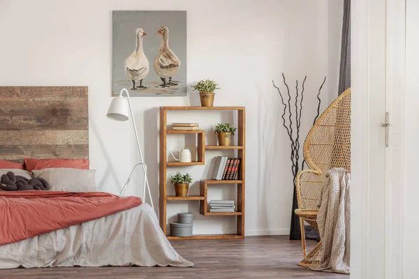 Foto real de um quarto rústico interior com uma pintura a óleo, estante de madeira e uma cama com lençóis vermelhos e brancos — Fotografia de Stock