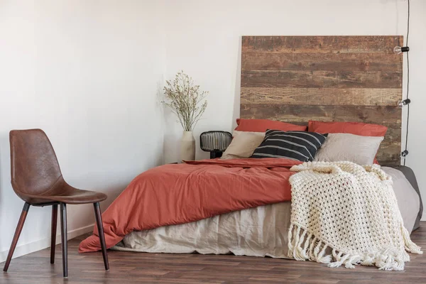 木製のベッド、白い壁とライトの文字列と自然なベッドルームのインテリアで革の椅子の実際の写真 — ストック写真