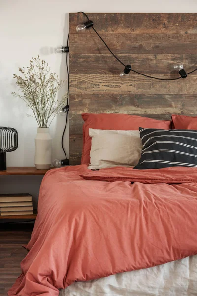 Close-up of lights hanging on a wooden bedhead in rustic bedroom interior with red sheets and black, striped pillow — Stock Photo, Image