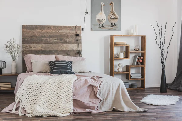 Couverture en maille beige sur un lit rose avec tête de lit en bois dans une chambre rustique intérieure pour une femme — Photo