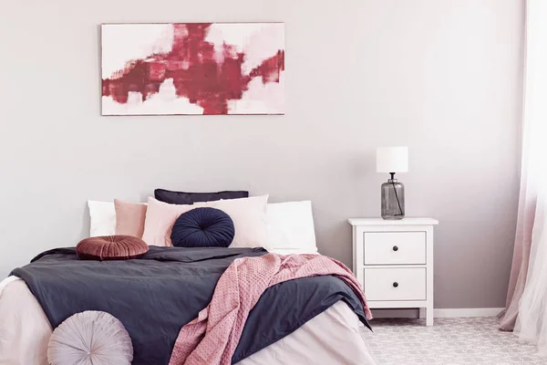 White lamp on wooden nightstand tale with drawers next to king size bed with round pillows and black duvet — Stock Photo, Image