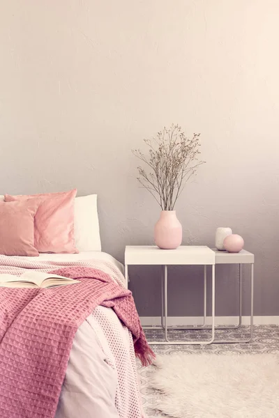 Flores secas en jarrón rosa pastel sobre una sencilla mesita de noche junto a la cama —  Fotos de Stock