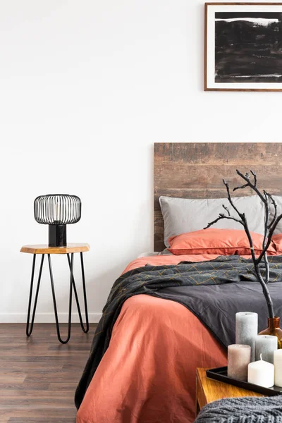 Industrial black lamp on wooden nightstand table nest to king size bed with orange and grey bedding — Stock Photo, Image