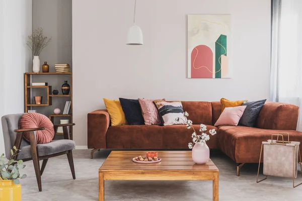 Blumen in Vase auf Holztisch im schicken Wohnzimmerinterieur mit braunem Ecksofa mit Kissen und abstrakter Malerei an der Wand — Stockfoto