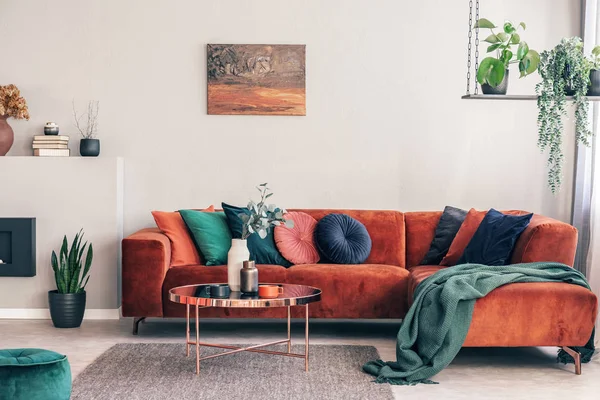 Mesa redonda elegante com flores ao lado do sofá de canto com travesseiros de esmeralda — Fotografia de Stock