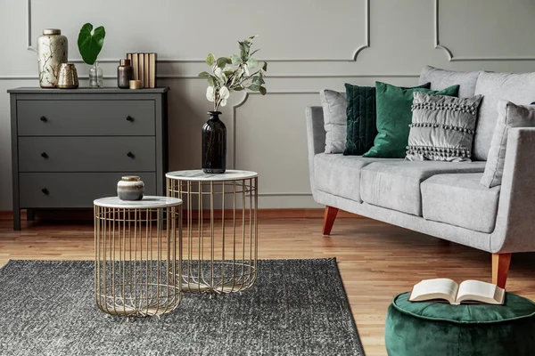 Zwei stylische kleine Couchtische mit Marmorplatten vor einer eleganten grauen Couch mit smaragdgrünen Kissen — Stockfoto