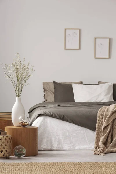 Wooden nightstand table next to king size bed with white and grey bedding in simple bedroom interior — Stock Photo, Image