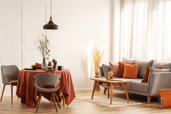 Интерьер гостиной и столовой с серым диваном и столом, покрытым оранжевой скатертью — стоковое фото
