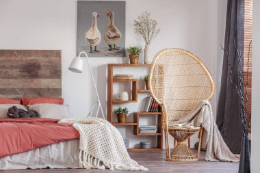 Kitaplık ve yatak başı ile kral boyutu yatak ile şık rustik yatak odasında battaniye ile Wicker tavus kuşu sandalye