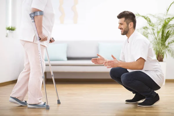 Seniorin im Krankenhaus lernt, wie man auf Knirpsen geht und unterstützt männliche Krankenschwester — Stockfoto
