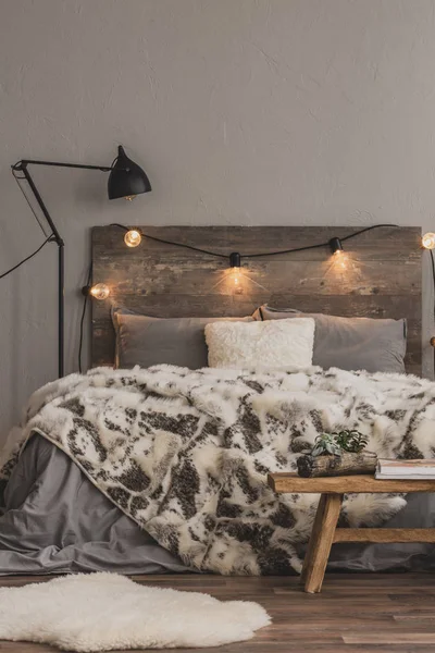 Industrial lamp and light bulbs on wooden headboard of comfortable bed with grey bedding and warm blanket — Stock Photo, Image