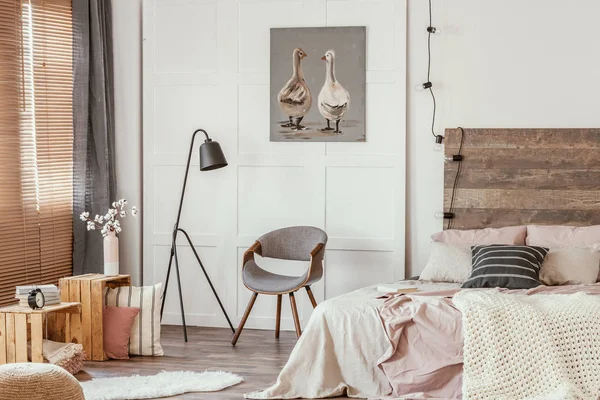 Zwarte industriële lamp naast stijlvolle grijze houten stoel in het midden van prachtige slaapkamer interieur — Stockfoto