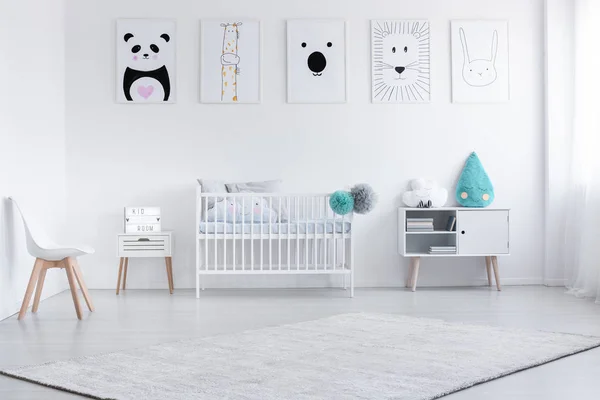 Carpet and chair in white simple child's room interior with posters on the wall above cradle. Real photo — Stock Photo, Image