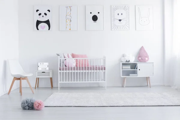 Pinkfarbene Kissen in Wiege und Stuhl im weißen Kinderzimmerinnenraum mit Postern und Teppich. echtes Foto — Stockfoto